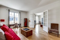 a study room with a second sofa, a study desk and table, chairs, and cabinets in a 2-bedroom Paris l