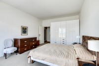 master bedroom is furnished with a queen-size bed, a large cabinet, a shelf, a nightstand, and two b
