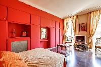 elegant bedroom with red walls and elegant gold accents with a queen-size bed, two armchairs, built-