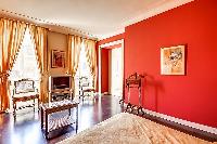 elegant bedroom with red walls and elegant gold accents with a queen-size bed, two armchairs, built-