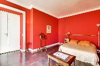 elegant bedroom with red walls and elegant gold accents with a queen-size bed, two armchairs, built-