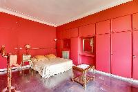 elegant bedroom with red walls and elegant gold accents with a queen-size bed, two armchairs, built-