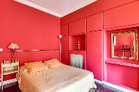 elegant bedroom with red walls and elegant gold accents with a queen-size bed, two armchairs, built-