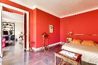 elegant bedroom with red walls and elegant gold accents with a queen-size bed, two armchairs, built-