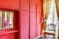 elegant bedroom with red walls and elegant gold accents with a queen-size bed, two armchairs, built-