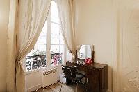 a dressing table with mirror and a chair tall windows, and drape curtains in a 1-bedroom Paris luxur