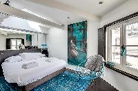 first bedroom in aqua, white and gray hues, furnished with a king-size bed with built-in shelves, an