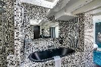 an en-suite bathroom with monochromatic mosaic tiles fully-furnished with a double sink, a mirror, a