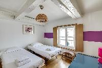 second bedroom in purple and fuschia hues furnished with two single beds, a few chairs, a desk, and 