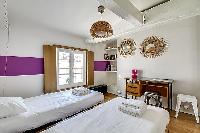 second bedroom in purple and fuschia hues furnished with two single beds, a few chairs, a desk, and 