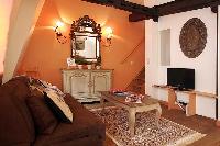 rustic living area with brown sofa, wooden table, cabinet, mirror, and lamps in a  2-bedroom Paris l