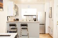 monochromatic and space-efficient kitchen with breakfast bar and stools in a 1-bedroom Paris luxury 
