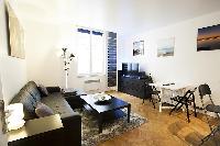 cozy living area with a media shelf, a television, a sleek center table, and a large, black sofa bed