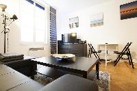 cozy living area with a media shelf, a television, a sleek center table, and a large, black sofa bed