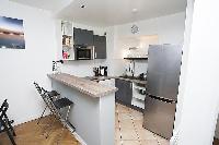 monochromatic and space-efficient kitchen with breakfast bar and stools in a 1-bedroom Paris luxury 