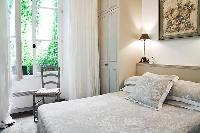 classy bedroom with built-in closets, lamps, chair, and queen-size bed  in Paris luxury apartment