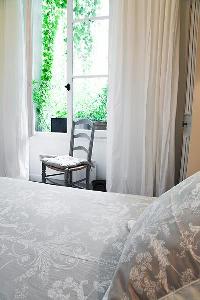 classy bedroom with  a chair, French window with potted plants and queen-size bed in Paris luxury ap