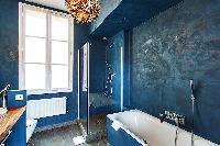 stylish bathroom in blue hue with a toilet, sink, shower, and a bathtub in a 3-bedroom Paris luxury 