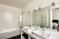immaculate white en-suite bathroom with double sink, mirror, and bathtub with detachable shower head