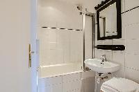 cozy bathroom with a bathtub, a sink, and a mirror in a 1-bedroom Paris luxury apartment