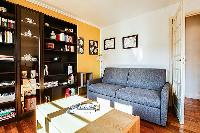 comfortable grey sofa bed, wooden center table, and shelves in a 1-bedroom Paris luxury apartment