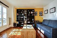 comfortable grey sofa bed, wooden center table, and shelves in a 1-bedroom Paris luxury apartment