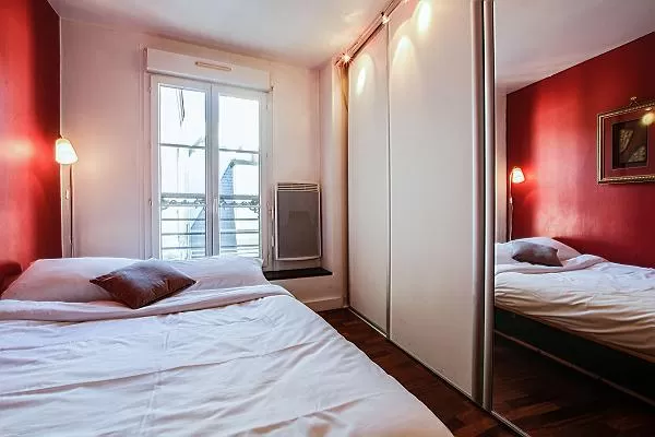 cozy bedroom with floor to ceiling mirrors, a hamper, and a queen-size bed in a 1-bedroom Paris luxu