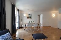 spacious dining area with floor lamp, wooden table and white chairs for six in a 2-bedroom Paris lux