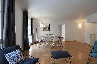 spacious dining area with floor lamp, wooden table and white chairs for six in a 2-bedroom Paris lux
