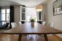 wooden dining table and white chairs for six, floor lamp, and bright window overlooking the street i