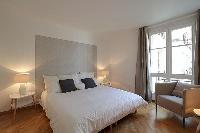 first bedroom with a king-size bed, bedside tables with lamps, and an armchair in a 2-bedroom Paris 