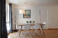 spacious dining area with floor lamp, wooden table and white chairs for six in a 2-bedroom Paris lux