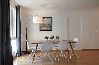 spacious dining area with floor lamp, wooden table and white chairs for six in a 2-bedroom Paris lux