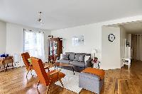 minimalist living room with a grey sofa bed, two apricot armchairs, a center table, and a cabinet wi