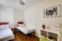 second bedroom with two single beds, a bedside table with lamp, storage drawers, and a cabinet in a 