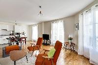 minimalist living room with a grey sofa bed, two apricot armchairs, a center table, and a cabinet wi