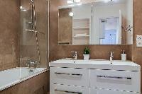 bathroom fully-equipped with double sinks, a bathroom cabinet, a mirror, and a bathtub with a detach
