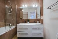 bathroom fully-equipped with double sinks, a bathroom cabinet, a mirror, and a bathtub with a detach
