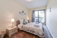 second bedroom with a queen-size bed, two bedside tables with lamps, a shelf with books, and French 