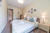 second bedroom with a queen-size bed, two bedside tables with lamps, a shelf with books