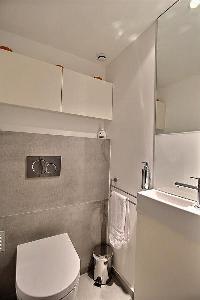 bathroom with a sink, bathroom shelves, a vanity mirror with lights, and shower area with a rainfall