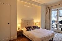 chic bedroom with a queen-size bed, built-in cabinets, bedside tables, lamps, drape curtain and tall