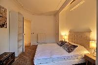 chic bedroom with a queen-size bed, shelves, chest, bedside tables, lamps, drape curtain and tall wi