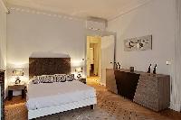 bedroom two with queen size bed, bdside tables, lamps, and ornamnetal fireplace in a Paris luxury ap