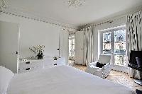 white bedroom three with queen size bed, armchair, TV and cabinet drawers in a Paris luxury apartmen