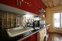 open kitchen in red hue with washer and dryer in a 1-bedroom Paris luxury apartment