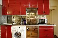 open kitchen in red hue with washer and dryer in a 1-bedroom Paris luxury apartment