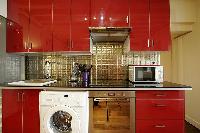 open kitchen in red hue with washer and dryer in a 1-bedroom Paris luxury apartment