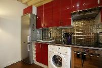 open kitchen in red hue with washer and dryer in a 1-bedroom Paris luxury apartment