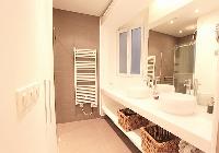 spacious bathroom with double sinks, bathroom shelves, wicker baskets, a mirror, and a shower area w